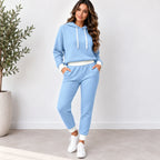 A woman modeling a light blue waffle-knit two-piece loungewear set consisting of a cropped hoodie and matching jogger pants, styled with white sneakers in a bright indoor setting.