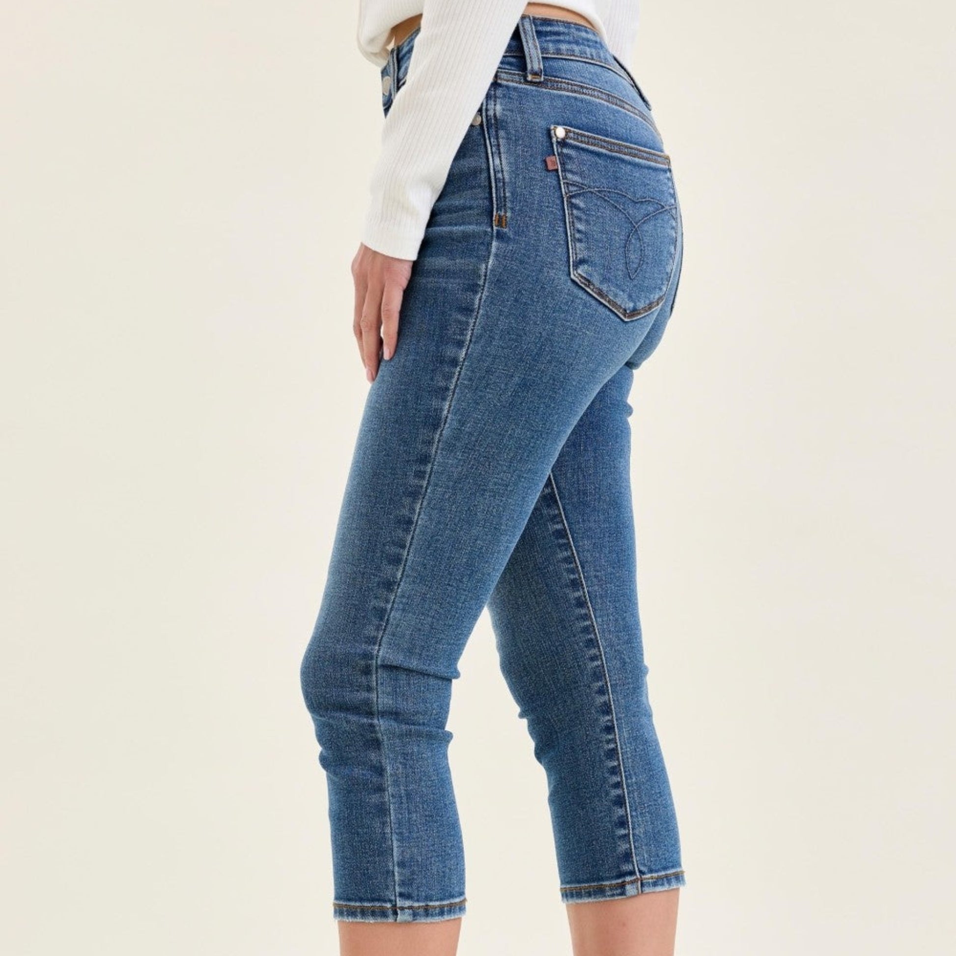 Close-up of the clean hem and slim leg opening on medium wash stretch denim capris.