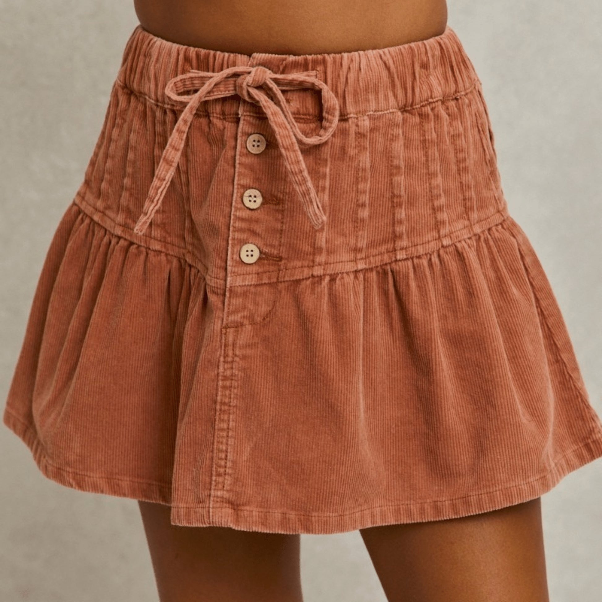 Close-up presentation of the SO ME rust mineral wash corduroy mini skirt with button details.