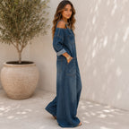 Side view of the Solazura Classic Wide Leg Denim Jumpsuit in navy blue featuring adjustable buckle straps, rolled long sleeves, oversized pockets, and a relaxed wide-leg fit.