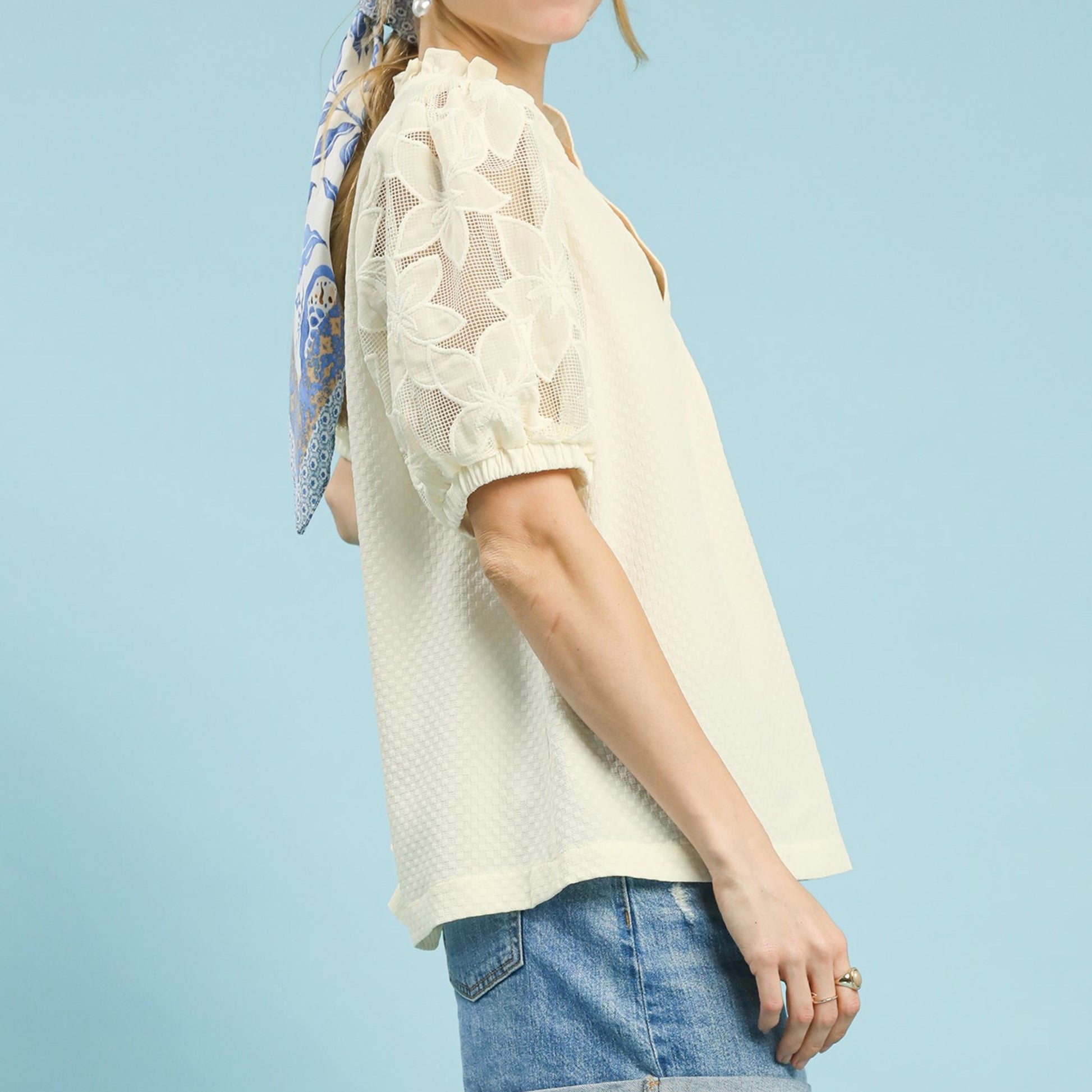 Detailed view of the notched neckline and textured fabric of the cream blouse.