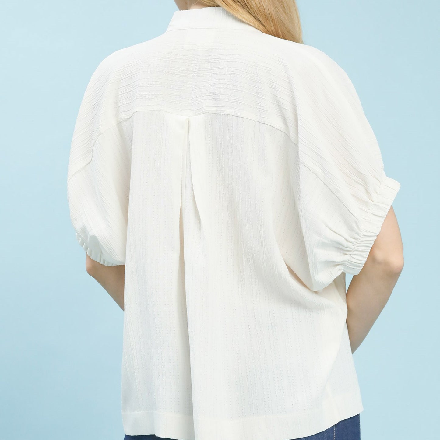 Back view of the women's cream textured blouse highlighting the flowy fit.