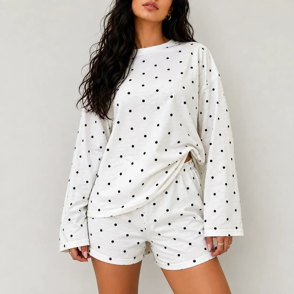 Model wearing white two-piece lounge set with black polka dots featuring long sleeves and relaxed shorts