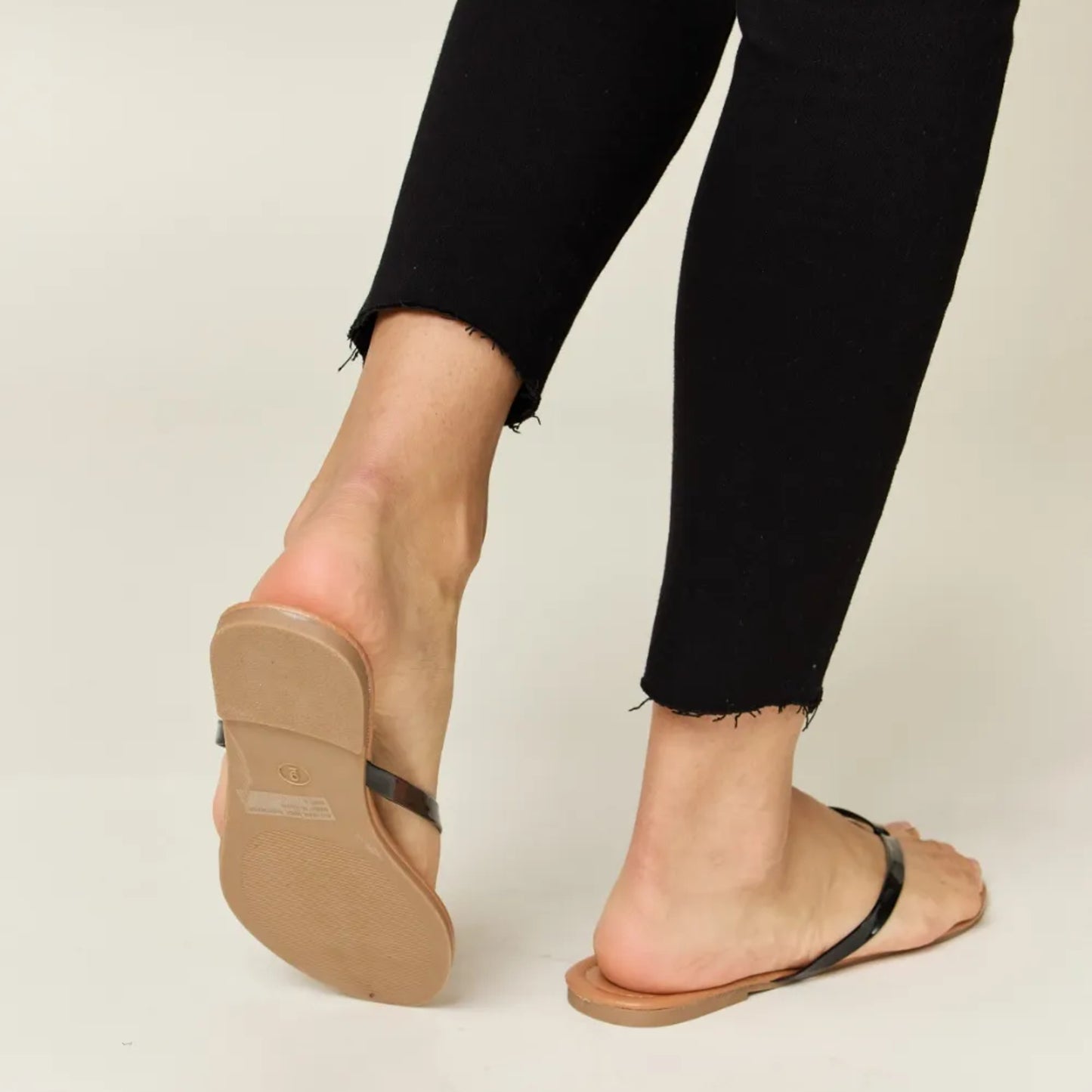 Person wearing tan sandals with black straps on a plain background