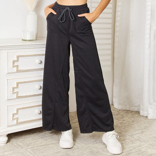 Person wearing dark gray wide-leg pants and white sneakers in a room with a white dresser and curtains.