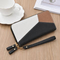A color-blocked zip-around wallet with a wrist strap, placed on a light wood tabletop next to a white teacup and saucer.