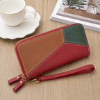 A geometric patchwork leather zip-around wallet with a wrist strap, styled on a light wood tabletop next to a white teacup and saucer.