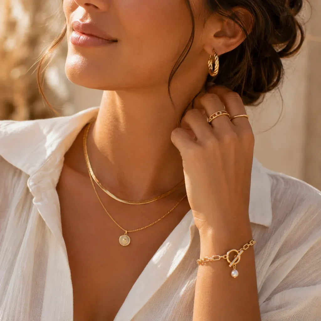 Woman wearing layered gold necklaces, hoop earrings, rings, and a bracelet for the women's jewelry collection at Solazura Boutique.